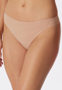 Sous-vêtements en thong nude fabriqués en tissu lisse et extensible. Présentent une taille basse et une couverture minimale avec un design épuré et sans coutures.