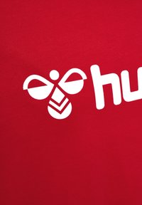 Röd bomulls-t-shirt med en vit grafik av en stiliserad bi ovanför ordet "hub." Designen inkluderar mjuka texturer och enkla former.