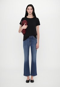 Tricou negru cu mânecă scurtă asortat cu blugi evazați din denim albastru. Ținând o geantă vișinie, purtând balerini negri, pe un fundal neutru.