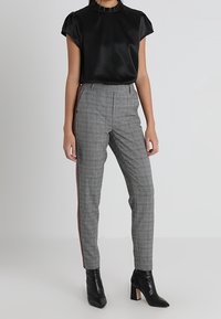 Svart satin topp med korta puffärmar, tillsammans med grå rutiga byxor med en röd sidrand, och svarta klackade ankelstövlar.