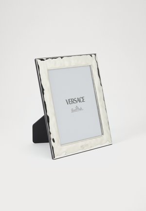 Foto lijst van zilverkleurig rechthoekig met een getextureerde rand, merklogo onderaan en een stevige zwarte standaard aan de achterkant.