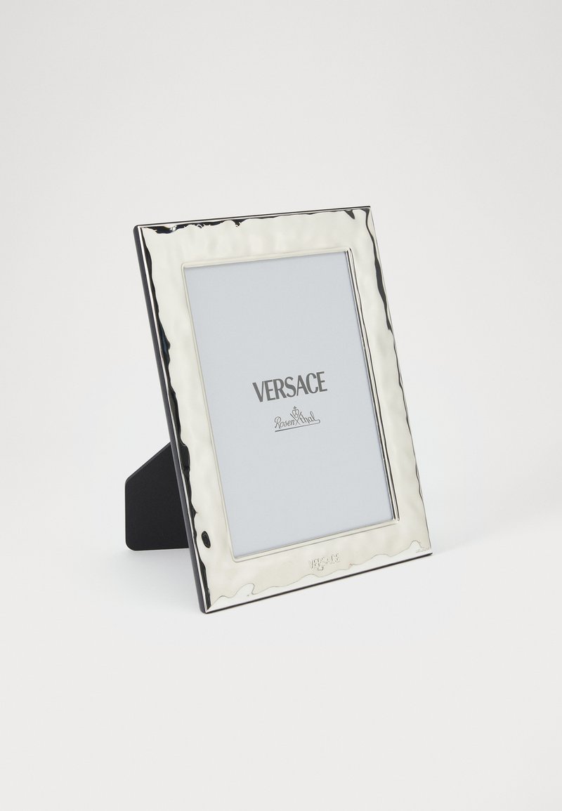 Rama foto dreptunghiulară cu nuanță argintie, cu margine texturată, logo-ul brandului în partea de jos și un suport negru robust în spate.