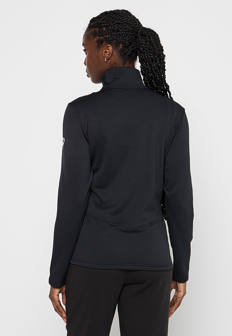 Schwarzes Langarmoberteil mit hohem Kragen, strukturiertem Stoff, taillierter Passform und abgerundetem Saum. Verfügt über ein kleines Logo am linken Ärmel.