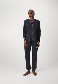 Marinblå pyjamasset i mjukt tyg som har en knapp-up skjorta med vita detaljer och raka byxor med uppvikta fållar.