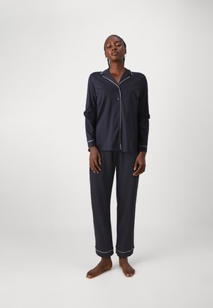 Marinblå pyjamasset i mjukt tyg som har en knapp-up skjorta med vita detaljer och raka byxor med uppvikta fållar.