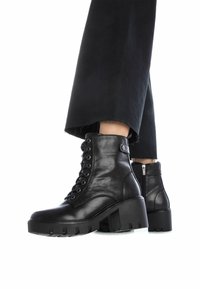 Botas de tobillo de cuero negro con cordones en la parte delantera y tacón ancho, con cremallera lateral y suela texturizada para un mejor agarre.