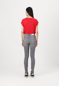 Camiseta roja de manga corta combinada con jeans ajustados grises. Los jeans tienen bolsillos traseros y un cinturón blanco, completando el atuendo con unos zapatos negros.