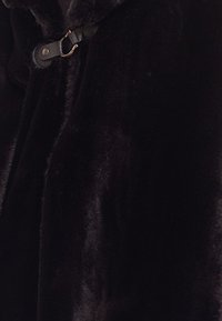 Svart faux fur-plagg med en mjuk, texturerad yta, utrustad med ett läderrem och metallspänne.