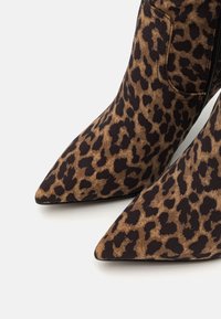 Bottes à bout pointu en tissu imprimé léopard marron et noir avec fermeture éclair latérale visible sur fond blanc.