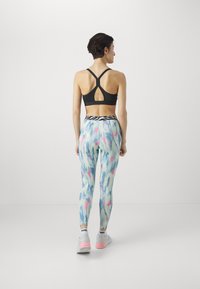 Fekete sportmelltartó, versenyhátsó kivitelben, színes, mintás leggingssel párosítva, amelyek pasztell kék, rózsaszín és fehér árnyalatokat tartalmaznak. Fehér edzőcipő, rózsaszín részletekkel.