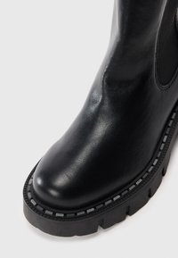 Zwarte leren enkelboot met een afgeronde neus, textuur oppervlak, chunky zwarte zool en contrasterende grijze stikdetails rond de basis.