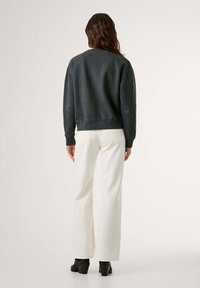 Felpa grigia scura con polsini e orlo a coste, abbinata a pantaloni bianchi a gamba larga e stivaletti neri con tacco. Design semplice, texture liscia.