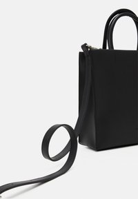 Svart läderhandväska med en strukturerad design, som har överhandtag och en justerbar axelrem. Slät yta och minimalistisk stil.
