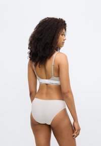 Γκρι βαμβακερό σουτιέν bralette με ρυθμιζόμενους ιμάντες και λάστιχο με το λογότυπο Calvin Klein, συνδυασμένο με ανοιχτό μπεζ seamless hipster εσώρουχο.