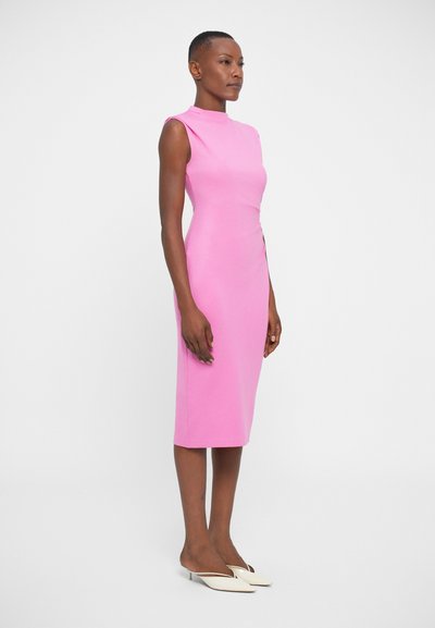 Úzké šaty po kolena v jasně růžové barvě, s vysokým výstřihem a bez rukávů. Nosené s krémovými podpatky. Hladká textura.