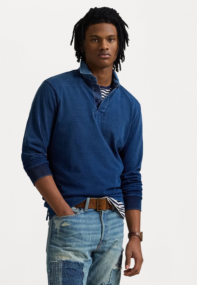 Marinblå tröja med denimkrage, ihop med slitna ljusblå jeans med lappar och ett brunt bälte. Randig topp under.