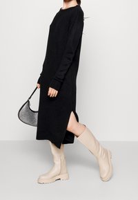 Černé dlouhé šaty s bočními rozparky, doplněné krémovými koženými kozačkami ke kolenům s robustní podrážkou a bočním zipem.