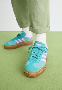 Tyrkysové semišové tenisky s ružovými pruhmi, štruktúrovaným zeleným jazykom a hnedou platformou, doplnené o biele rebrované ponožky.