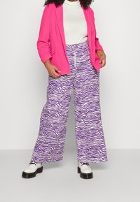 Blazer rosa brillante, dolcevita bianca e pantaloni a gamba larga con stampa zebra viola. Scarpe con plateau bianche stringate completano l'outfit.