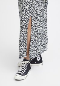 Lång, mönstrad klänning i vitt och marinblått med en sidoklyvning; ihop med svarta högsneakers från Converse med vita detaljer.