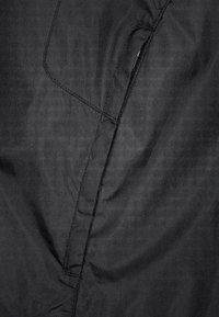 Tejido negro con una textura suave, que presenta una costura y una cremallera oculta. El material tiene un brillo sutil, que resalta su diseño ligero.