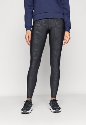 Leggings noires avec un motif floral subtil, texture lisse, taille haute, associées à des chaussures de sport noir et blanc.