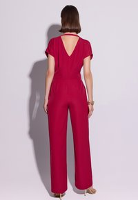 Różowy kombinezon malinowy z krótkimi rękawami, dekoltem w kształcie litery V z tyłu, dopasowaną talią i szerokimi spodniami, wykonany z gładkiego materiału.