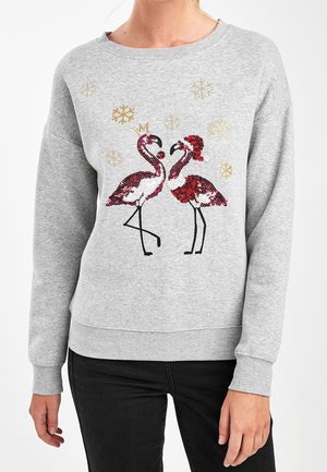Sweat-shirt gris avec deux flamants roses pailletés se faisant face, l'un portant une couronne, l'autre un bonnet de Père Noël, entourés de flocons de neige dorés.
