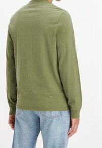 Olivgrön långärmad skjorta i bomull, med rundad halsringning och avslappnad passform, ihop med ljusblå denimjeans.