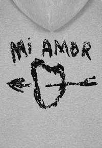 Felpa grigia con stampa nera che recita "Mi Amor" e un design di un cuore con una freccia. Il materiale sembra morbido e informale.