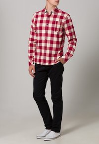 Rood-wit geruite blouse met lange mouwen en een knoopsluiting kraag, gecombineerd met zwarte broek en witte sneakers.