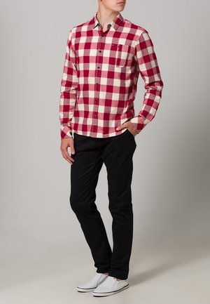 Camicia a maniche lunghe a quadri rossi e bianchi con colletto abbottonato, abbinata a pantaloni neri e sneaker bianche.