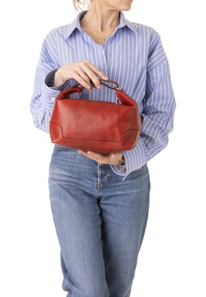 Femme en chemise à rayures bleues et jean tenant un sac à main en cuir rouge avec une poignée courte au niveau de la taille.