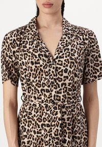Leopardų rašto marškinėlių suknelė su trumpomis rankovėmis ir mygtukų užsegimu, su juosmens diržu ir lygiu, lengvu audinio tekstūra.
