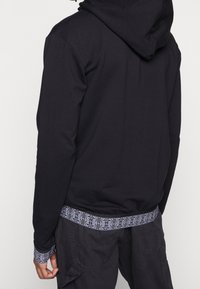 Sudadera negra con un acabado texturizado y cordones ajustables. Puños y dobladillo con un diseño geométrico. Corte casual.