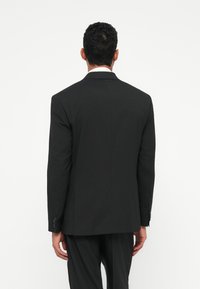 Chaqueta de traje negra con un corte ajustado, una abertura trasera, solapas con muesca y tres botones en cada puño. Tela suave, diseño minimalista.