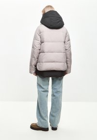 Puff jakken har en lys grå krop med en sort hætte, quiltet design og afslappet pasform. Den er parret med løse blå jeans og brune sko.
