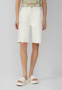 Shorts en denim blanc taille haute, avec une coupe classique, cinq poches et des détails de couture minimaux. Associés à des sandales à plateforme blanches.