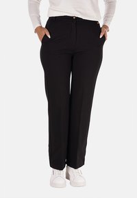 Pantaloni neri su misura con una texture liscia, design a gamba dritta, tasche frontali e bottoni dorati, abbinati a sneakers bianche.