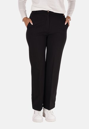 Pantaloni neri su misura con una texture liscia, design a gamba dritta, tasche frontali e bottoni dorati, abbinati a sneakers bianche.