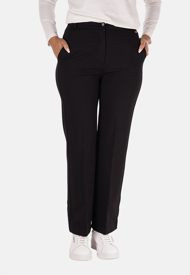Pantaloni neri su misura con una texture liscia, design a gamba dritta, tasche frontali e bottoni dorati, abbinati a sneakers bianche.