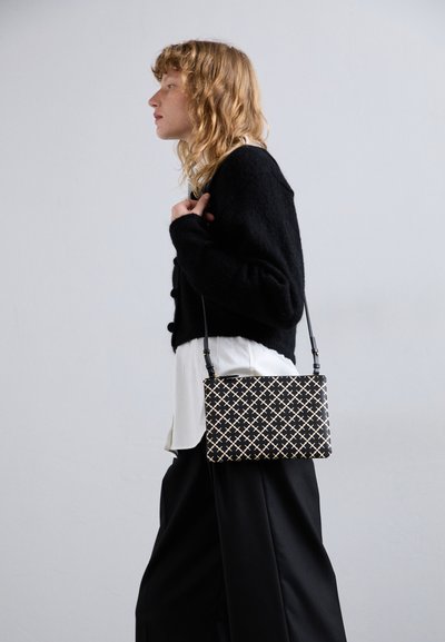 Borsa a tracolla nera e crema a motivo, dalla forma rettangolare, con una tracolla removibile e una superficie texture, indossata sopra una camicia bianca.