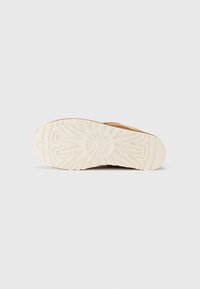Tan rubber shoe sole with a patterned tread design, featuring a white midsole. Bottom view emphasizes texture and grip detail.