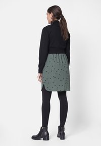 Czarny krótki sweter, zielona sukienka w czarne kropki, z bocznymi rozporkami, w połączeniu z czarnymi legginsami i botkami za kostkę z złotymi akcentami.