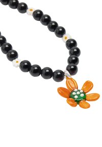 Czarny naszyjnik z koralików z małymi białymi kwiatowymi akcentami oraz pomarańczowym wiszącym kwiatem z zielonym środkiem i białymi kropkami.