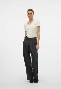 Witte top met korte mouwen en een ronde hals, gecombineerd met hoge, losse donkergrijze broek met plooien en knoopsluiting.
