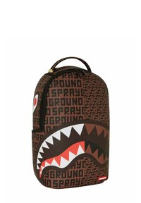 Mochila marrón con un diseño de boca de tiburón con dientes rojos, acentuada por el texto repetido "SPRAYGROUND" en negro. Cierre de cremallera en la parte superior.