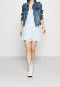 Ljusblommig klänning med omslag, lager på lager av tyg, bärs under en mörk denimjacka. Vita högsnobb sneakers fulländar looken.