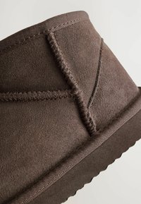 Gros plan sur une botte en daim marron présentant une couture et une semelle texturée, mettant en avant son matériau doux et son design décontracté.