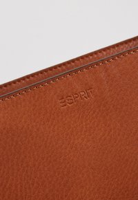 Cartera de cuero marrón texturizado con el logo "ESPRIT" en relieve, con bordes cosidos y un diseño liso y elegante.
